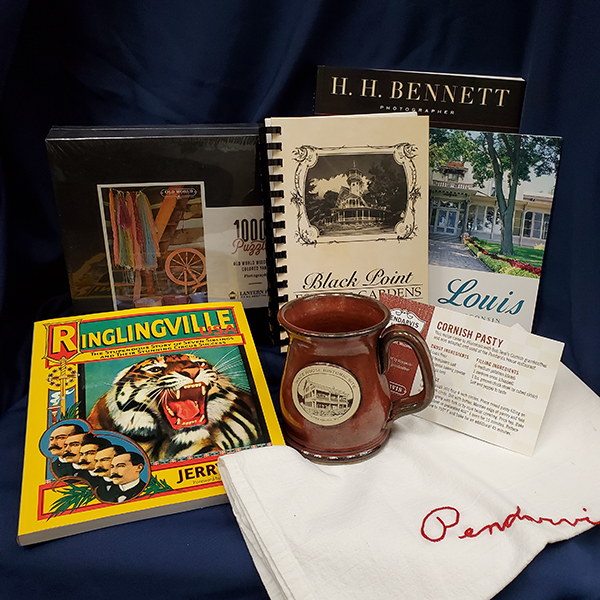 A 1000 piece puzzle, Pendarvis tea towels featuring a cornis pasty recipe, Ringlingville USA book by Jerry Apps, a photographed brown mug, and Black Point Estate and H.H. Bennett book.